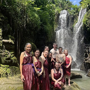 A group of  students and staff in traditional Indonesian clothing standing in front of a waterfall