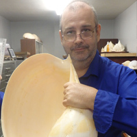Master of Philosophy alumni Stephen Maxwell wearing a blue shirt and holding up a large shell
