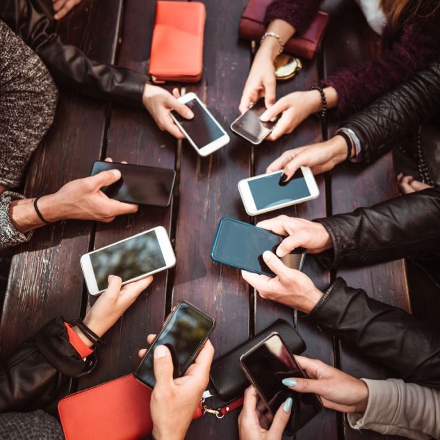 Seven people's hands gathered around a table each holding phones. 